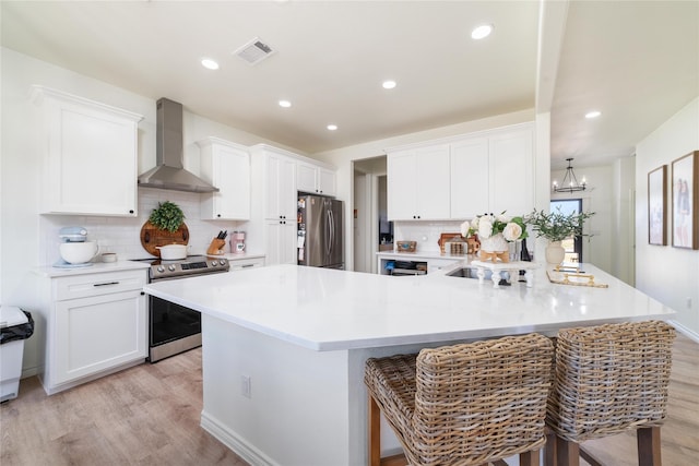 kitchen featuring stainless steel appliances, visible vents, light wood-style flooring, and wall chimney exhaust hood