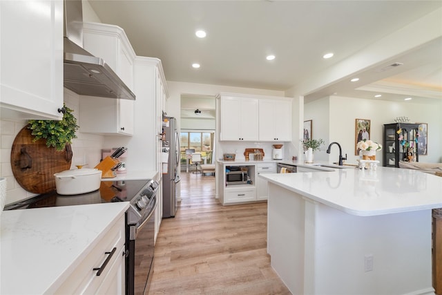 kitchen with stainless steel appliances, backsplash, light wood-style flooring, and wall chimney exhaust hood