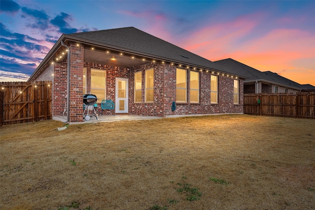 back of house featuring a patio area, a yard, a fenced backyard, and brick siding