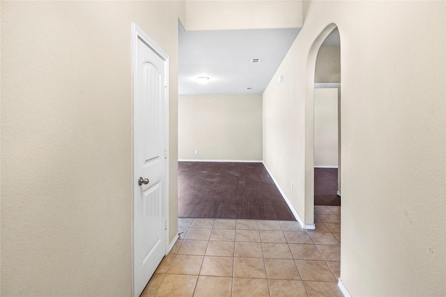 hallway with arched walkways, light tile patterned flooring, visible vents, and baseboards