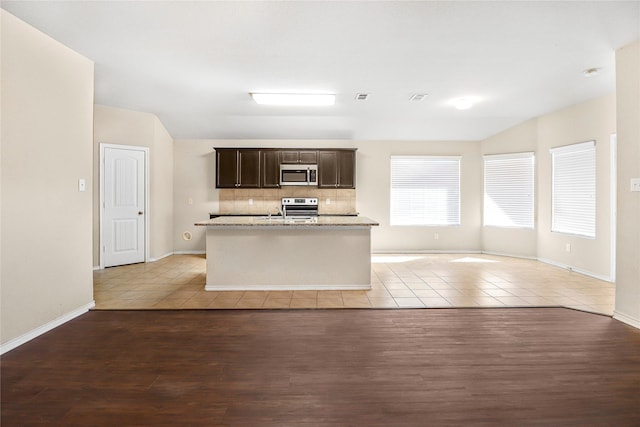 302 Triple Crown Ln, Ponder, TX 76259 - kitchen featuring a center island with sink, light tile patterned floors, stainless steel appliances, backsplash, and dark brown cabinetry