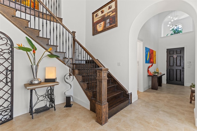 entrance foyer with baseboards, a high ceiling, arched walkways, and stairs