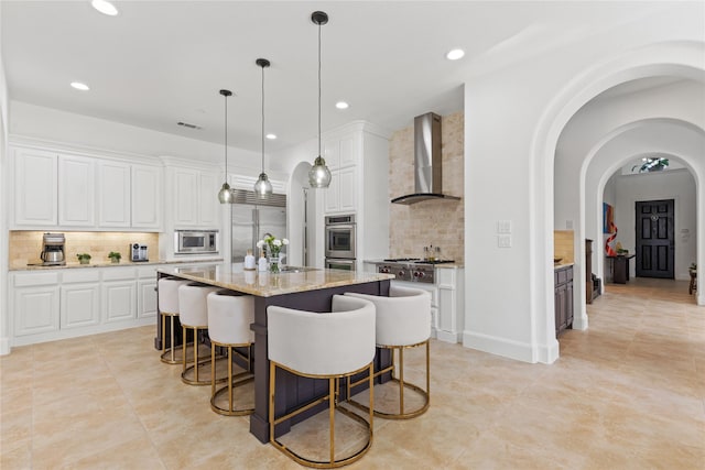 kitchen with white cabinetry, a kitchen island, a sink, wall chimney range hood, and built in appliances