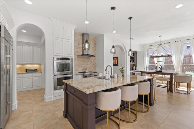 kitchen featuring backsplash, appliances with stainless steel finishes, white cabinetry, a sink, and wall chimney exhaust hood