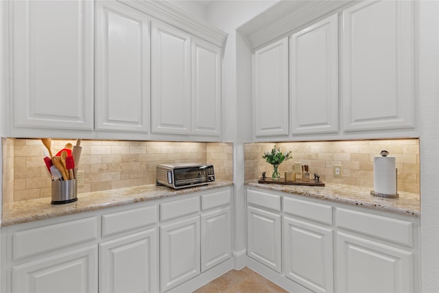 kitchen with light tile patterned floors, a toaster, tasteful backsplash, white cabinets, and light stone counters