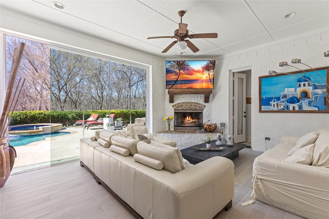 living room with ceiling fan, an outdoor stone fireplace, and wood finished floors