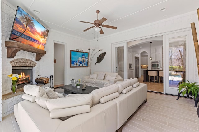 living area with a fireplace, arched walkways, and a ceiling fan