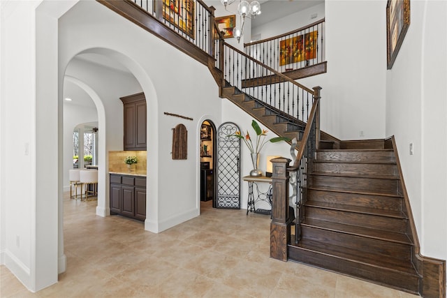 staircase with a chandelier, arched walkways, baseboards, and a high ceiling