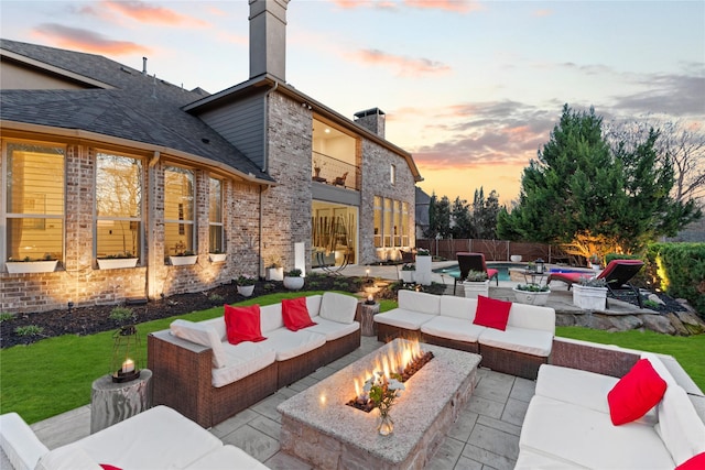 patio terrace at dusk with a yard, fence, and an outdoor living space with a fire pit