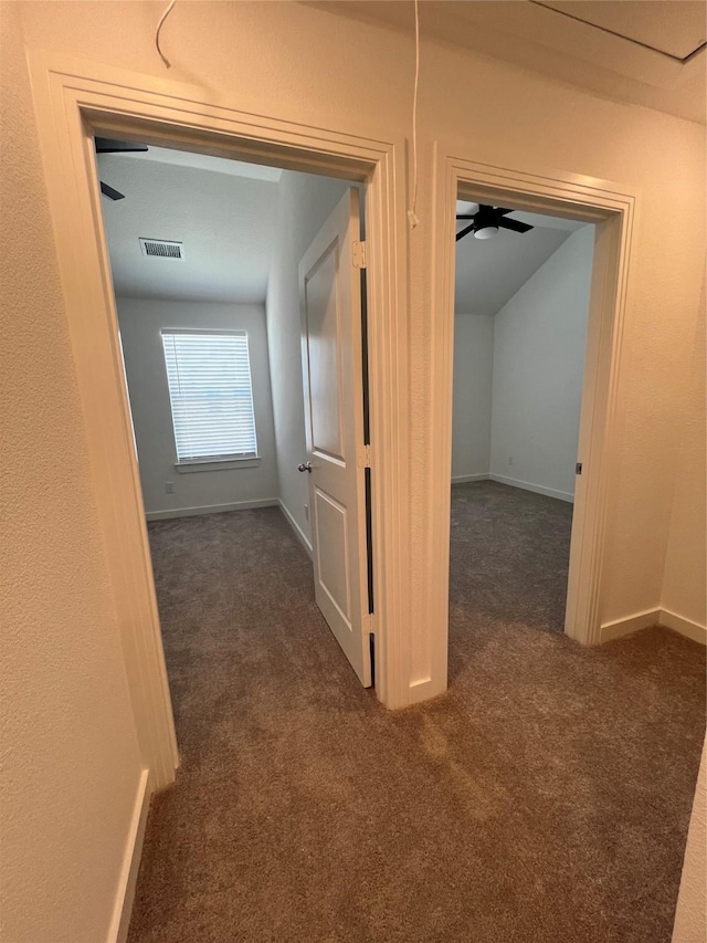 hallway featuring attic access, visible vents, baseboards, and dark colored carpet