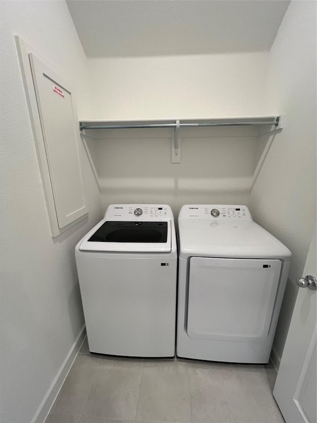 clothes washing area featuring laundry area, light tile patterned floors, baseboards, and washer and dryer