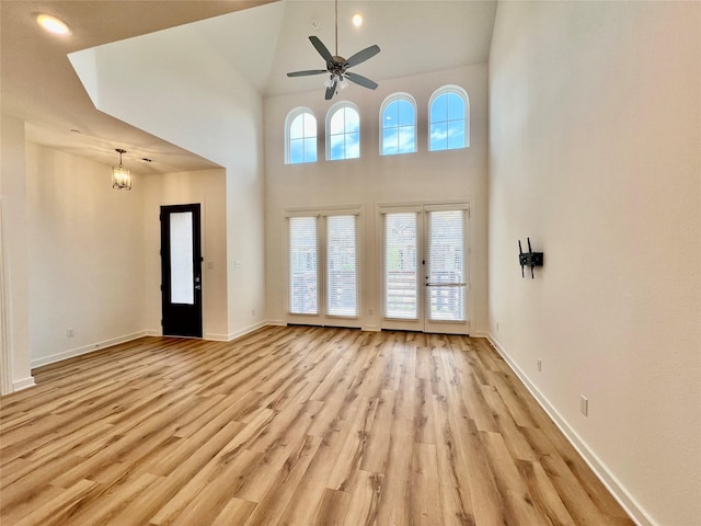 interior space featuring light wood finished floors, a high ceiling, a ceiling fan, and baseboards