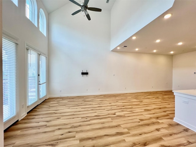 unfurnished living room featuring a wealth of natural light, a high ceiling, ceiling fan, and light wood finished floors