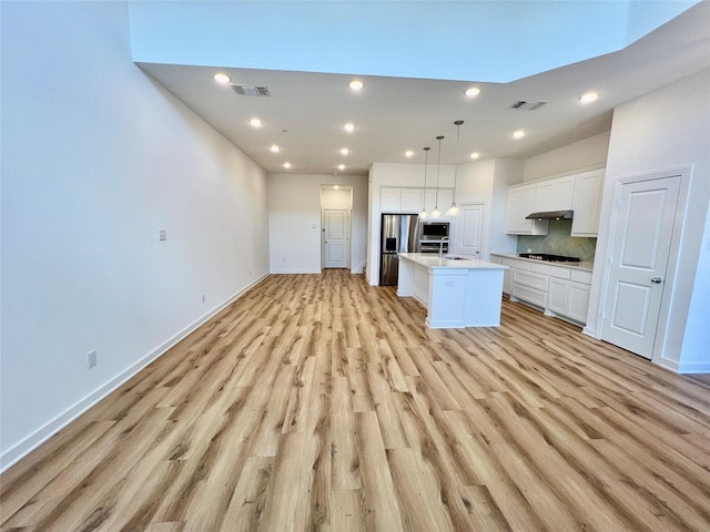 kitchen with appliances with stainless steel finishes, open floor plan, visible vents, and an island with sink