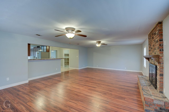 unfurnished living room featuring a brick fireplace, visible vents, baseboards, and wood finished floors