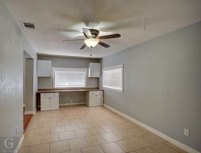 kitchen with a ceiling fan, baseboards, visible vents, white cabinetry, and built in study area