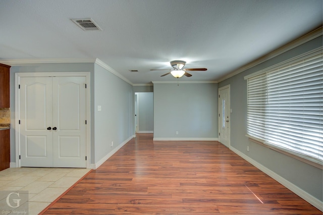 spare room with a ceiling fan, light wood-style floors, visible vents, baseboards, and ornamental molding