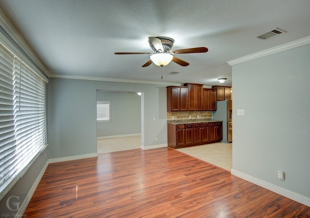 unfurnished living room with light wood-type flooring, a ceiling fan, visible vents, and crown molding