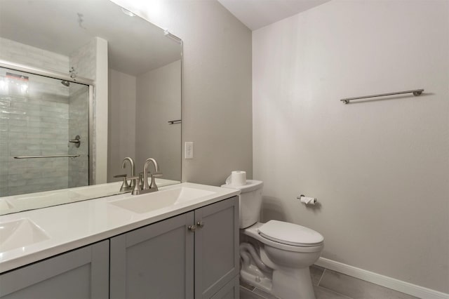 bathroom featuring double vanity, toilet, a stall shower, a sink, and baseboards