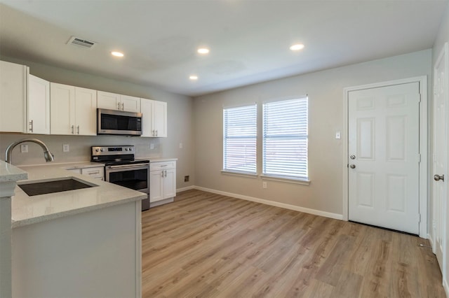 kitchen with visible vents, white cabinets, appliances with stainless steel finishes, light wood-style floors, and a sink