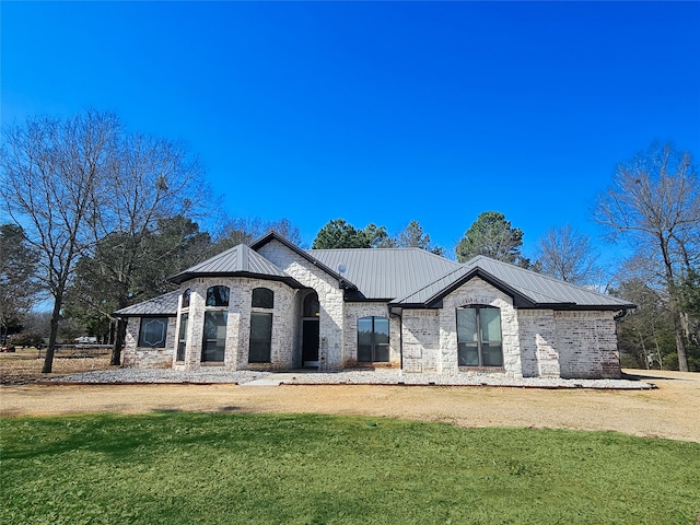 french country style house with a standing seam roof, brick siding, metal roof, and a front lawn