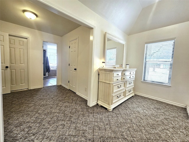 hallway featuring lofted ceiling, dark colored carpet, plenty of natural light, and baseboards