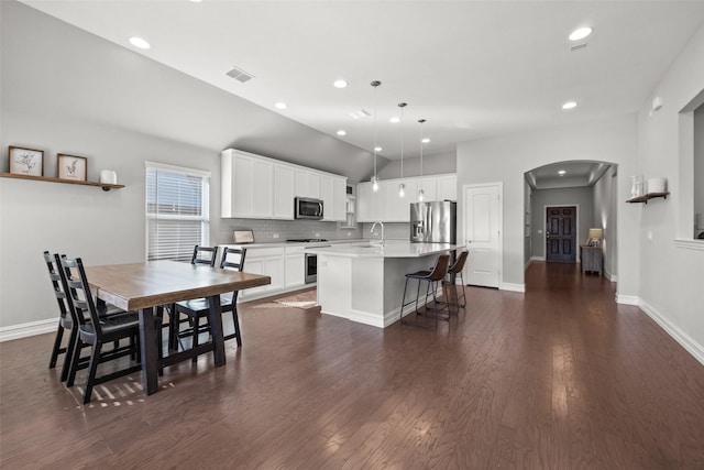 kitchen with arched walkways, stainless steel appliances, light countertops, backsplash, and a kitchen island with sink