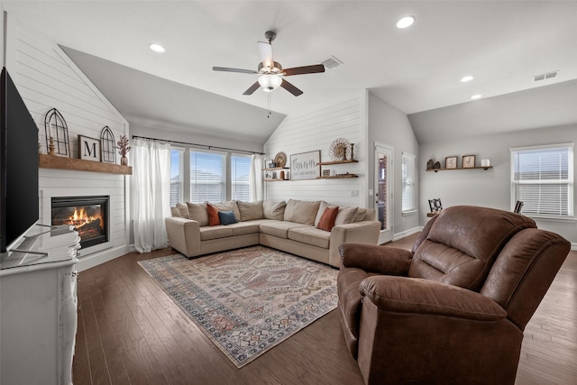 living room featuring dark wood-style flooring, visible vents, vaulted ceiling, and a large fireplace