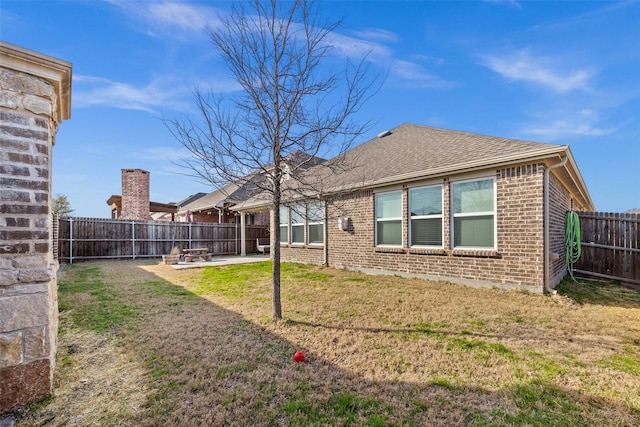 back of property with a fenced backyard, brick siding, a shingled roof, a yard, and a patio area