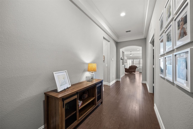 hallway featuring arched walkways, visible vents, baseboards, ornamental molding, and dark wood-style floors