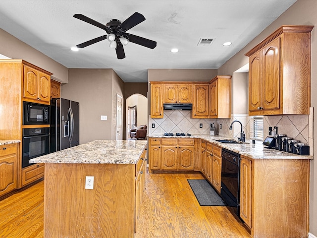 kitchen featuring visible vents, arched walkways, a kitchen island, black appliances, and a sink