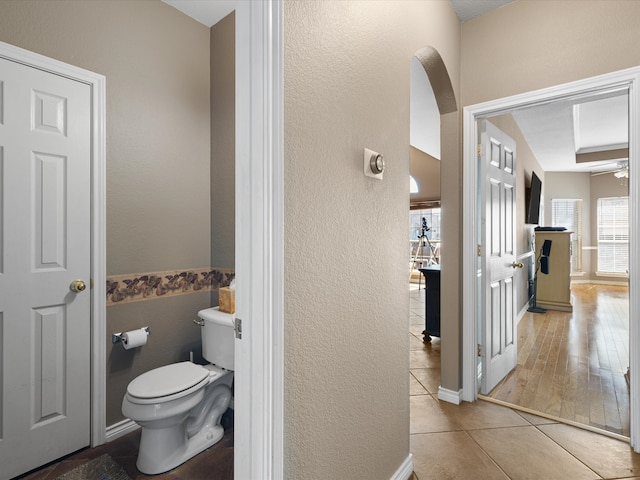 bathroom with a textured wall, tile patterned flooring, ceiling fan, and toilet