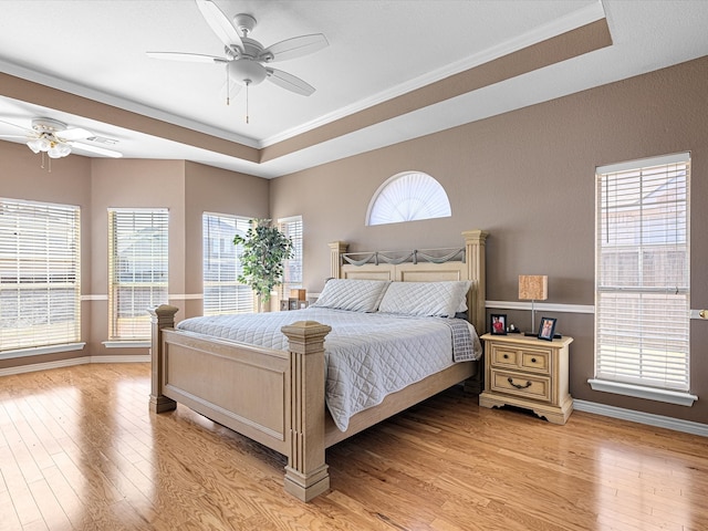 bedroom with light wood-type flooring, a ceiling fan, a tray ceiling, and crown molding