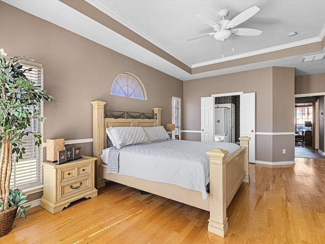 bedroom featuring light wood-style floors, a tray ceiling, baseboards, and crown molding