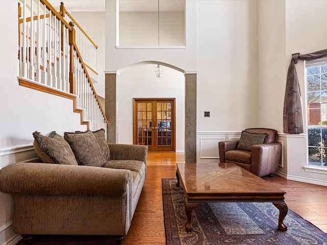 living area with arched walkways, wood finished floors, a high ceiling, stairs, and french doors