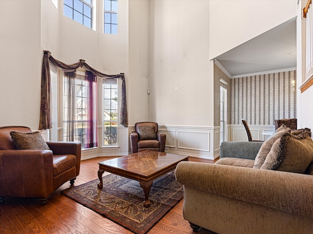 living area with hardwood / wood-style flooring, a decorative wall, a towering ceiling, wainscoting, and crown molding