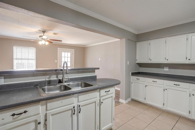 kitchen with dark countertops, ornamental molding, white cabinets, and a sink