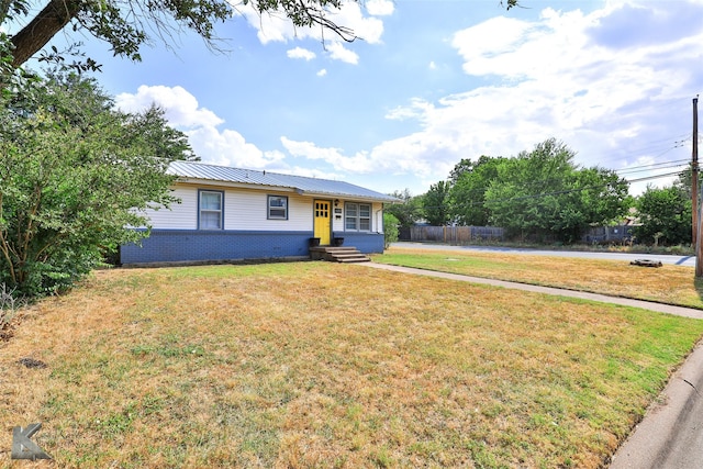 view of front of house with entry steps, brick siding, metal roof, and a front lawn