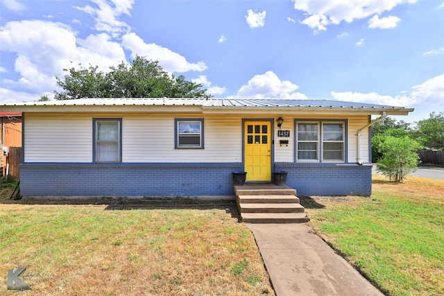 view of front of property featuring entry steps, metal roof, brick siding, and a front lawn