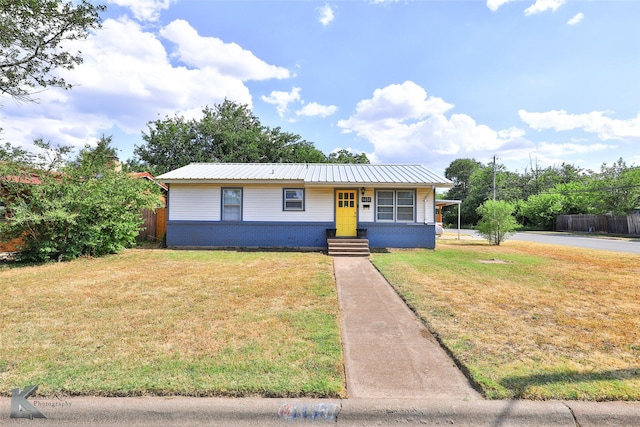 view of front of property featuring metal roof, brick siding, a front lawn, and fence