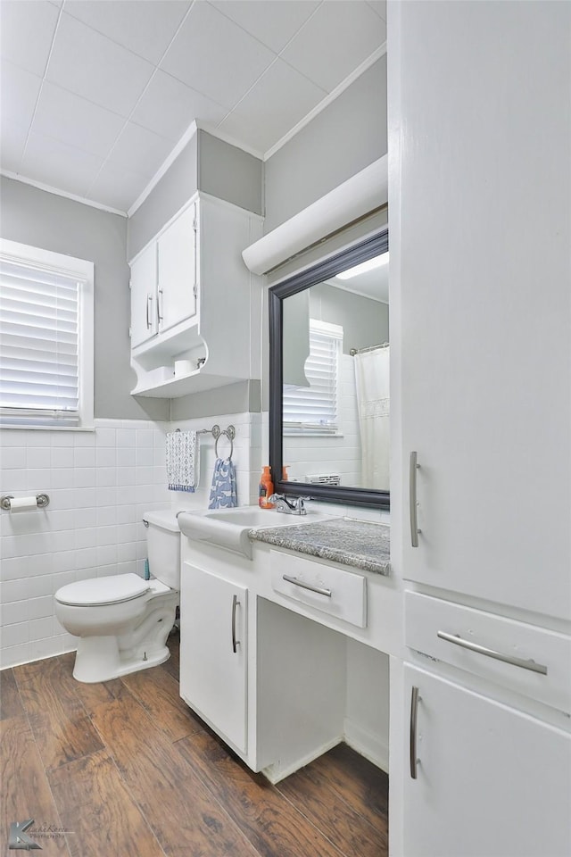 bathroom with tile walls, toilet, ornamental molding, vanity, and wood finished floors