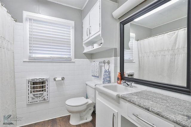 full bath featuring toilet, wood finished floors, heating unit, vanity, and tile walls