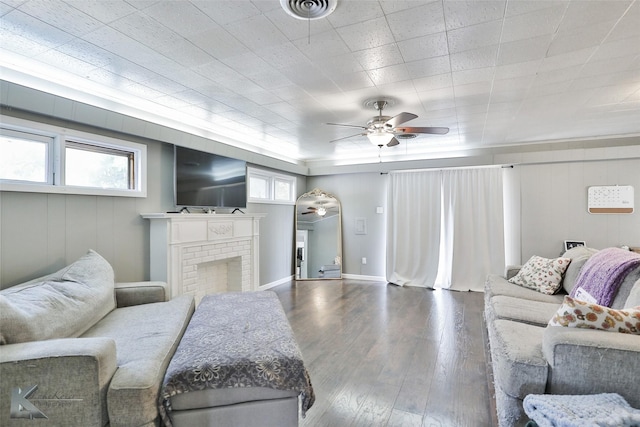 living area featuring a brick fireplace, visible vents, ceiling fan, and wood finished floors