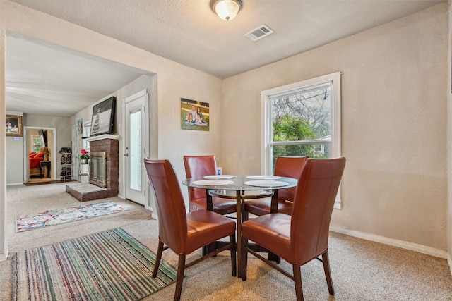 dining area featuring a textured ceiling, carpet flooring, visible vents, baseboards, and a brick fireplace