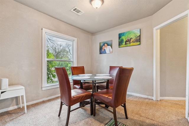 dining room with a textured ceiling, light colored carpet, visible vents, and baseboards