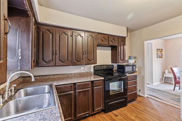 kitchen featuring light wood finished floors, dark brown cabinetry, a sink, a textured ceiling, and black appliances