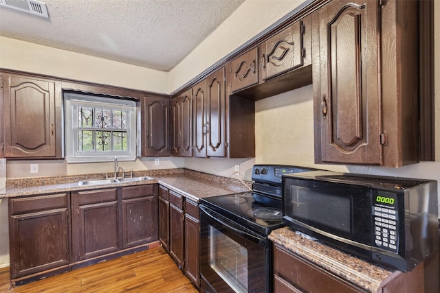 kitchen featuring visible vents, light wood-style flooring, dark brown cabinets, black appliances, and a sink