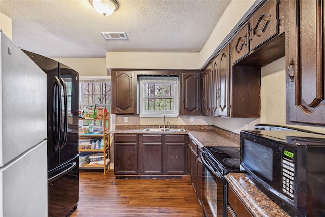 kitchen with dark wood-type flooring, a sink, visible vents, dark brown cabinets, and black appliances