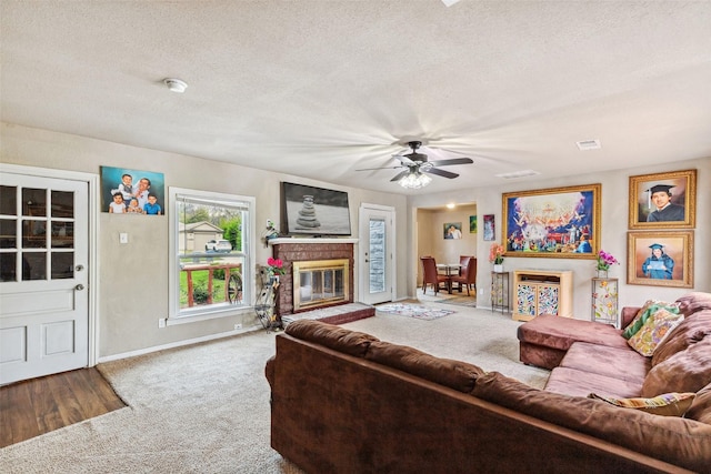 living room featuring visible vents, ceiling fan, a textured ceiling, carpet flooring, and a brick fireplace