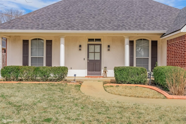 view of exterior entry featuring a shingled roof, a yard, and stucco siding